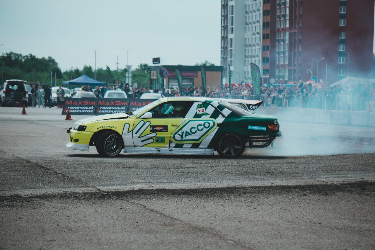 services-01 A car drifts on an asphalt track, leaving a trail of smoke during an outdoor racing event.